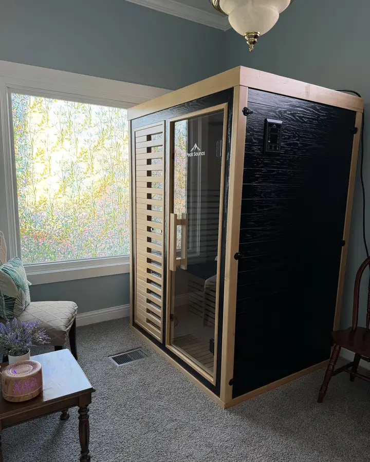 The Full-Spectrum sauna cabin in pale wood and dark panelling, beside a window and a small side table.