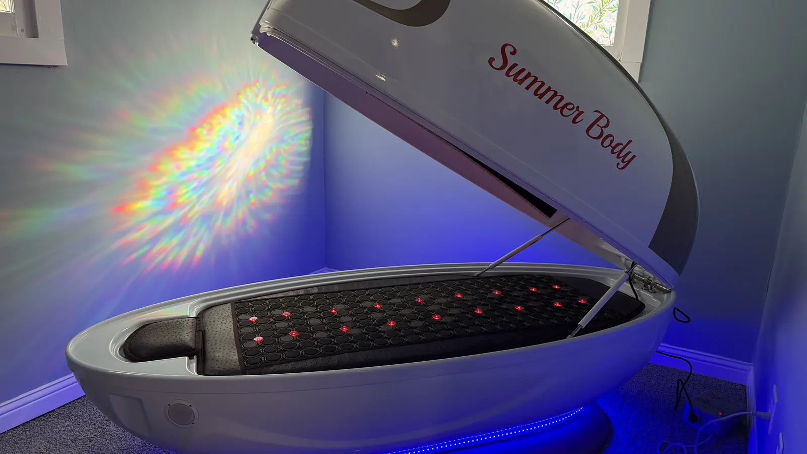 The Summer Body Pod with its lid raised, the red-light bed lit inside and a blue glow beneath it.